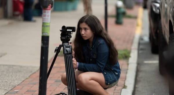 A young person positions a camcorder on a tripod