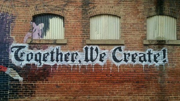 Mural on brick with gothic text: "Together, We Create"