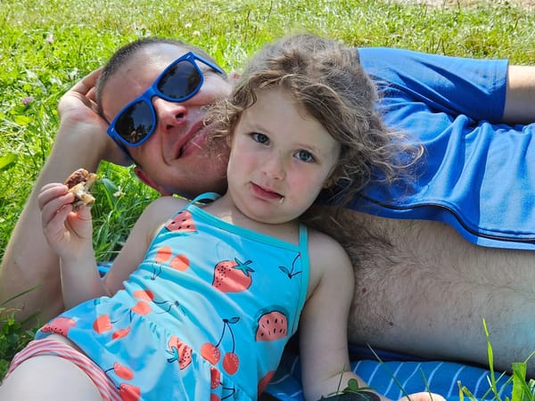 Girl in swimsuit leans back on adult in unzipped bike jersey