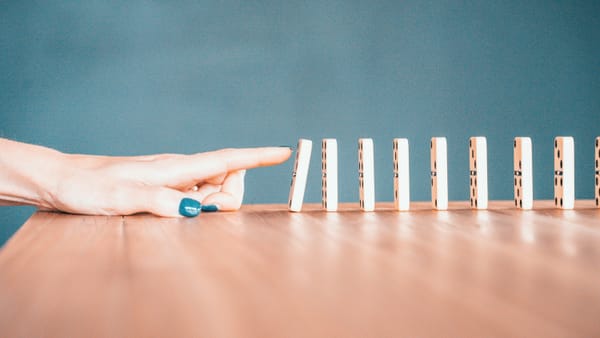 Finger poised to knock over the first in a line of dominos